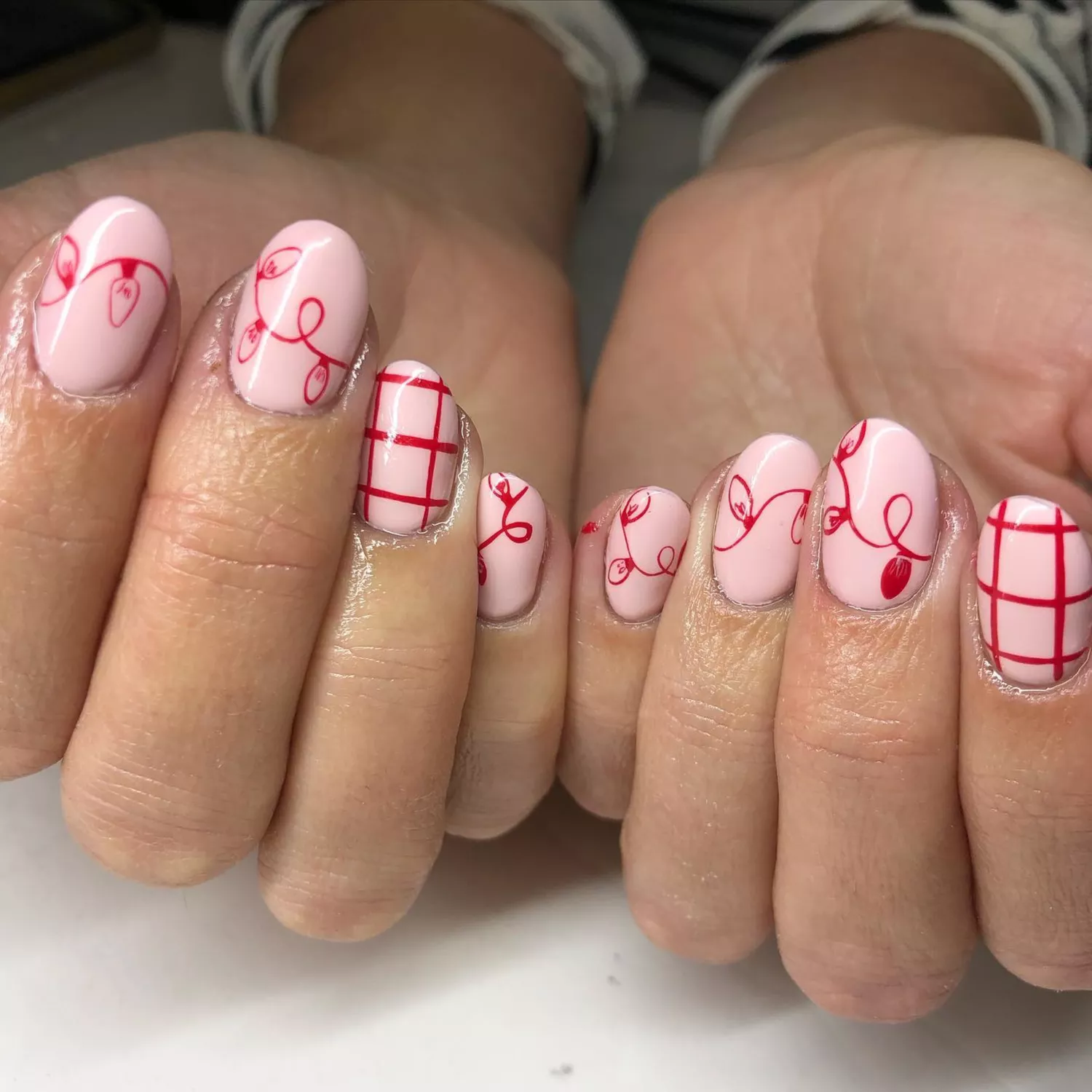 Pink based manicure with red string light and plaid nail art.